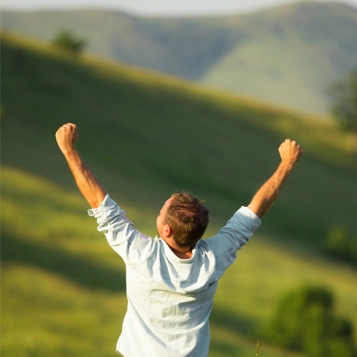 Person with arms raised in triumph against a lush green landscape, symbolizing emotional breakthrough and renewed vitality from Ketamine IV Therapy for depression, anxiety, and PTSD.
