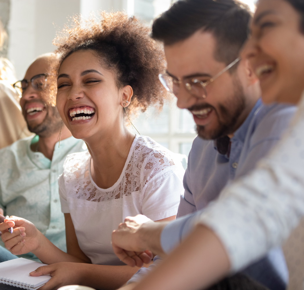 Four people seated together in a sunlit room, smiling and laughing in a moment of connection. Featured on the Mind Rejuvenation Home page to reflect joy, community, and the uplifting power of mental wellness.