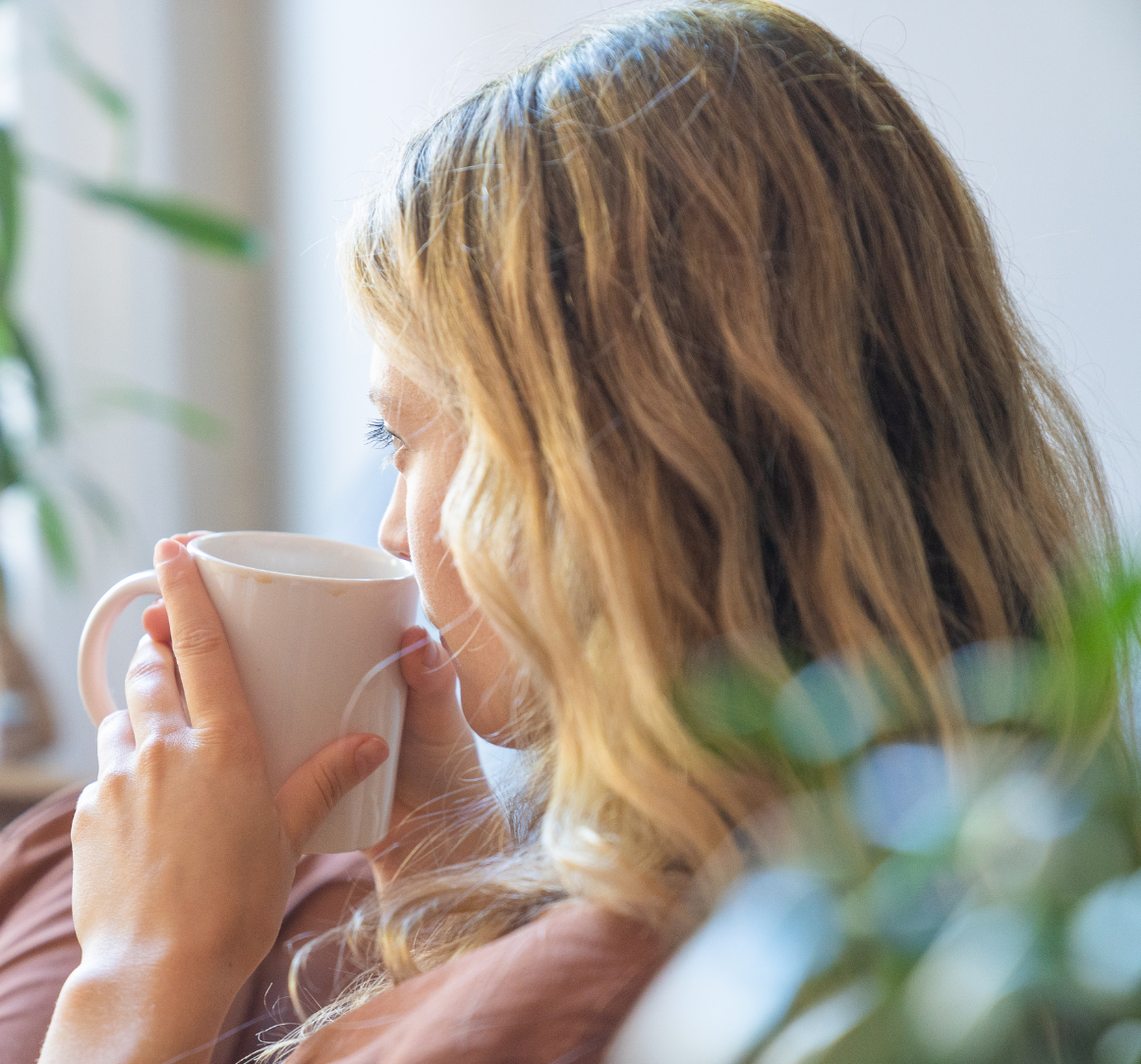 Relaxed woman sipping from a white mug in a sunlit room with plants—evoking calm, self-care, and the emotional healing supported by SPRAVATO treatment at Mind Rejuvenation.