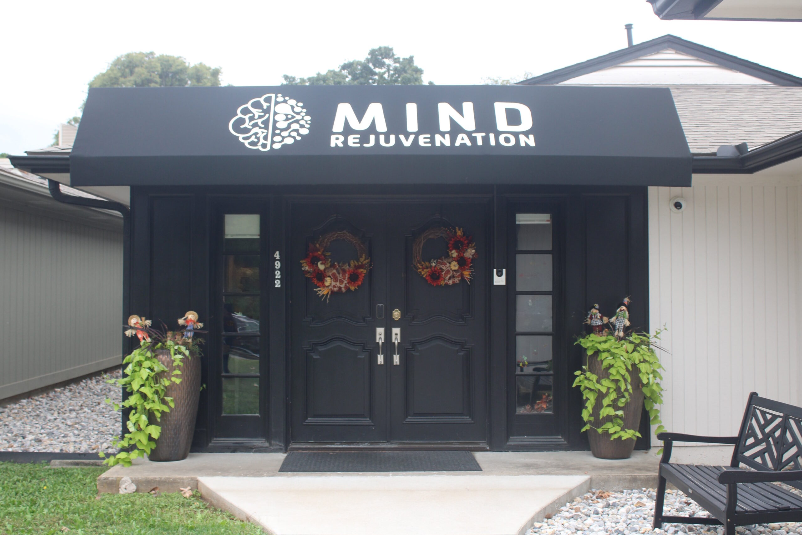 Entrance to the Mind Rejuvenation building with black double doors, autumn wreaths, and a bold awning featuring the logo and name. Featured on the About page in the What to Expect section to convey warmth, professionalism, and a welcoming space for mental wellness.