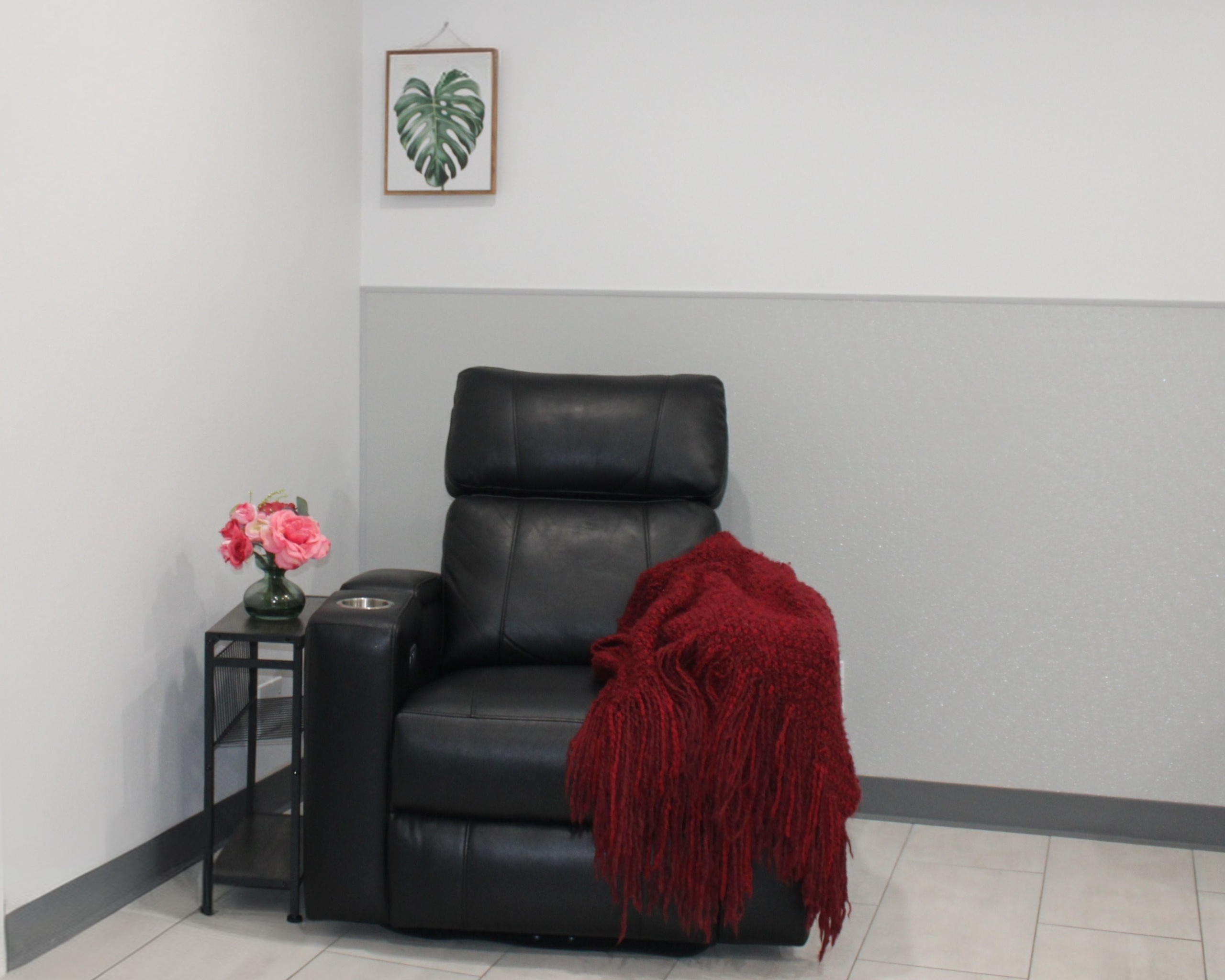 Cozy room corner with a black leather recliner draped in a deep red throw, beside a side table with pink and red flowers. Featured on the Mind Rejuvenation Home page to evoke comfort, calm, and a welcoming space for mental wellness.